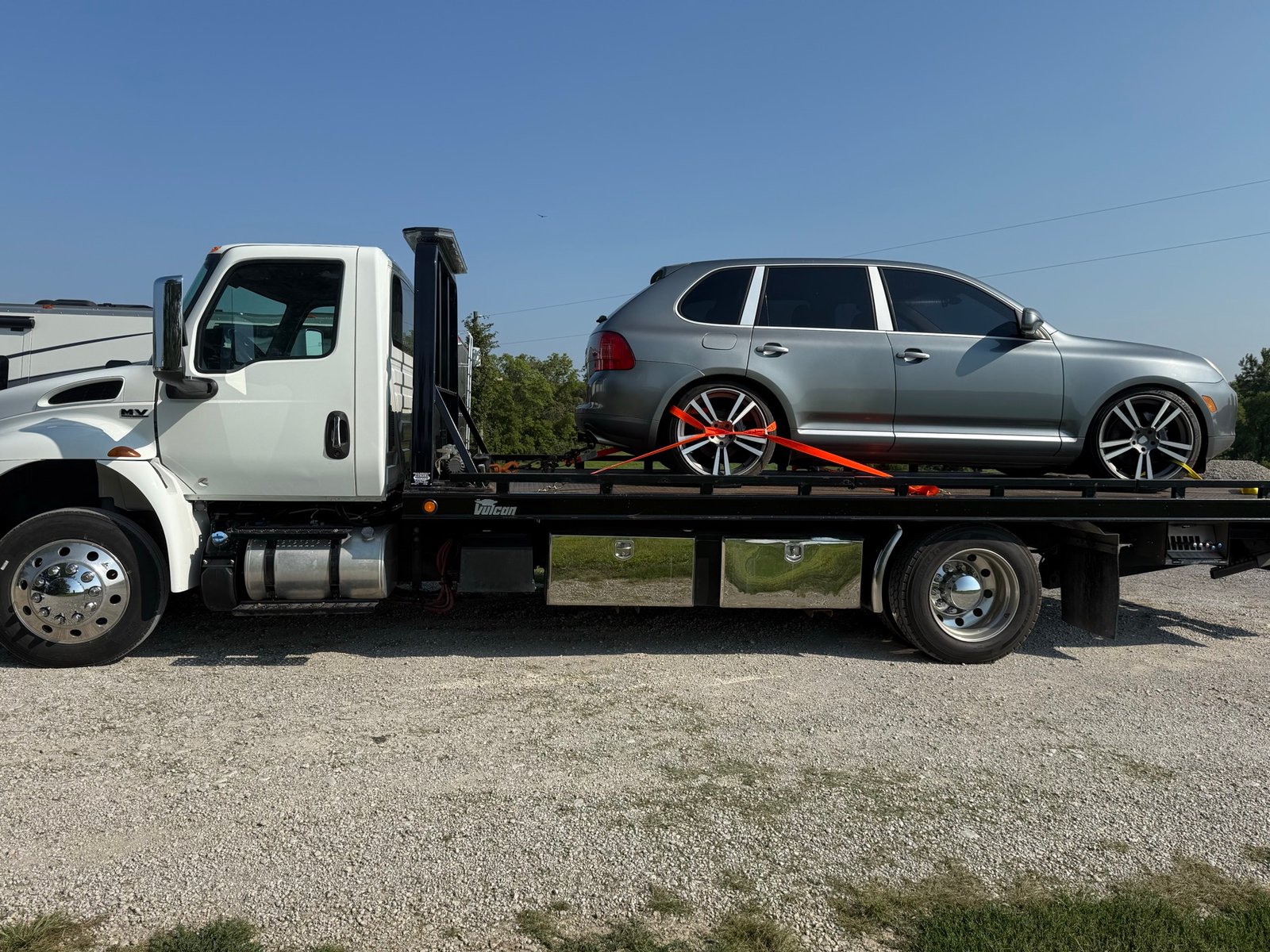An AMS Vulcan flatbed carrying a silver Porsche Cayenne secured with soft straps