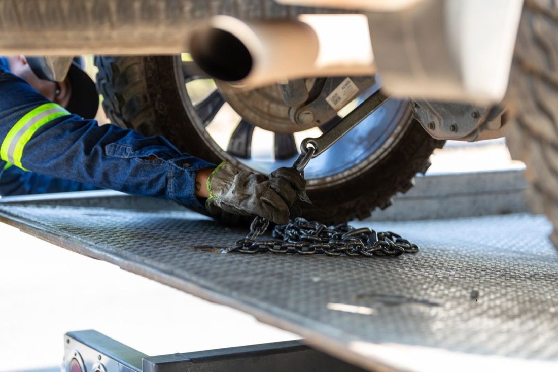 A tow operator securing a vehicle with chains on a flatbed